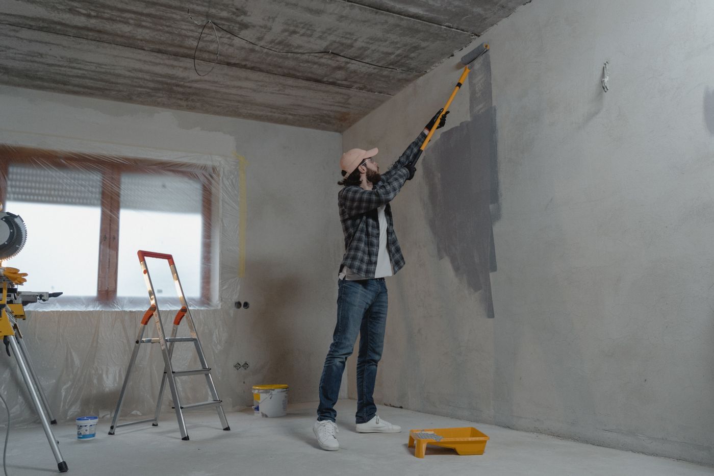 Man verft een grijze muur met een verfroller op lange steel